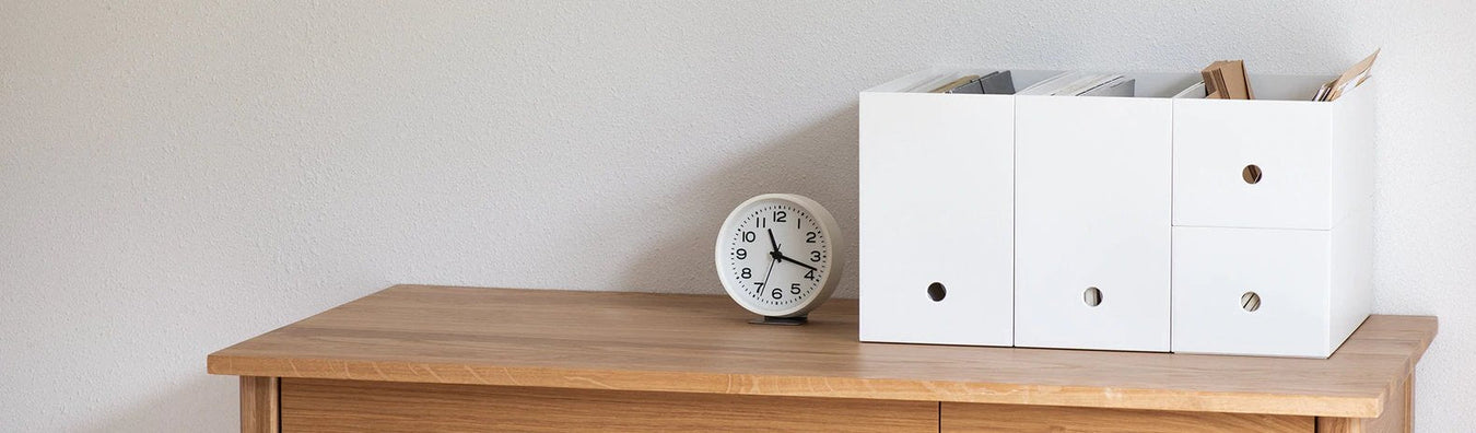 Wood Desk with a white clock next to white file storage containers.