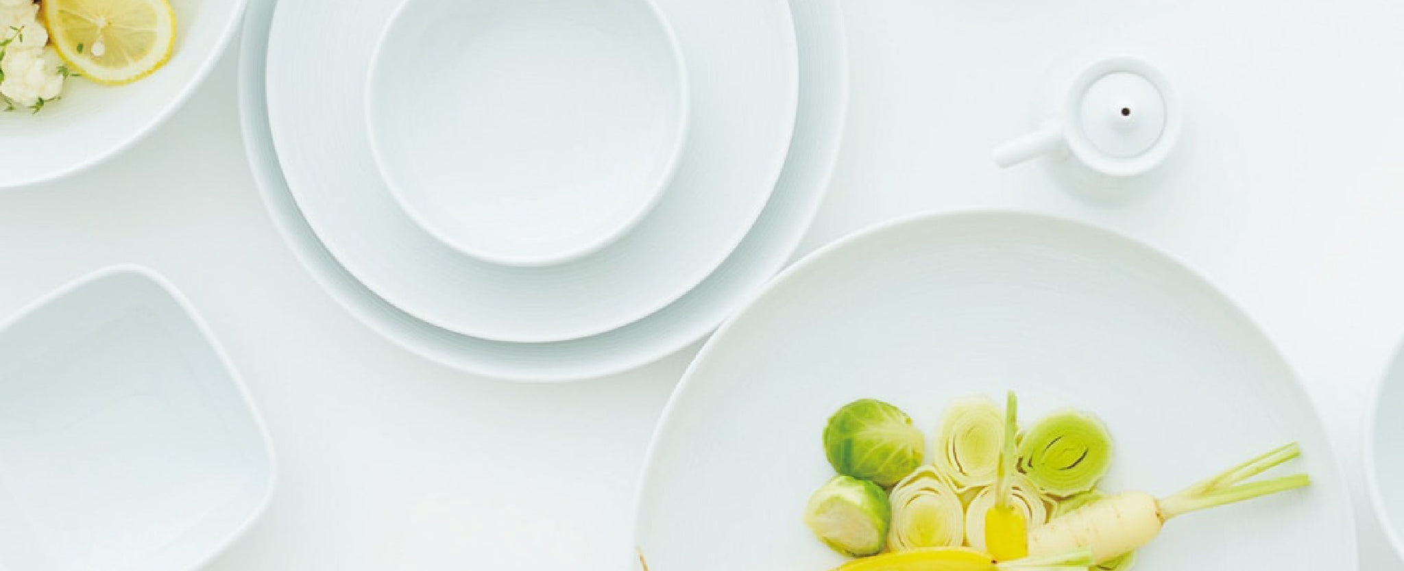 Various White Plates and Bowls on a White Background.  The bowl in the foreground has roots and sprouts in it. 