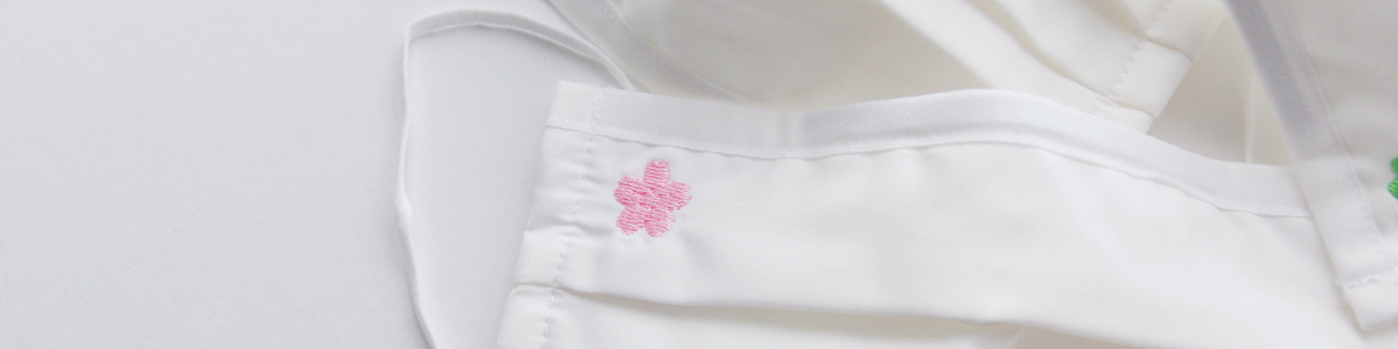 White mask with an embroidered small pink flour embellishment. 