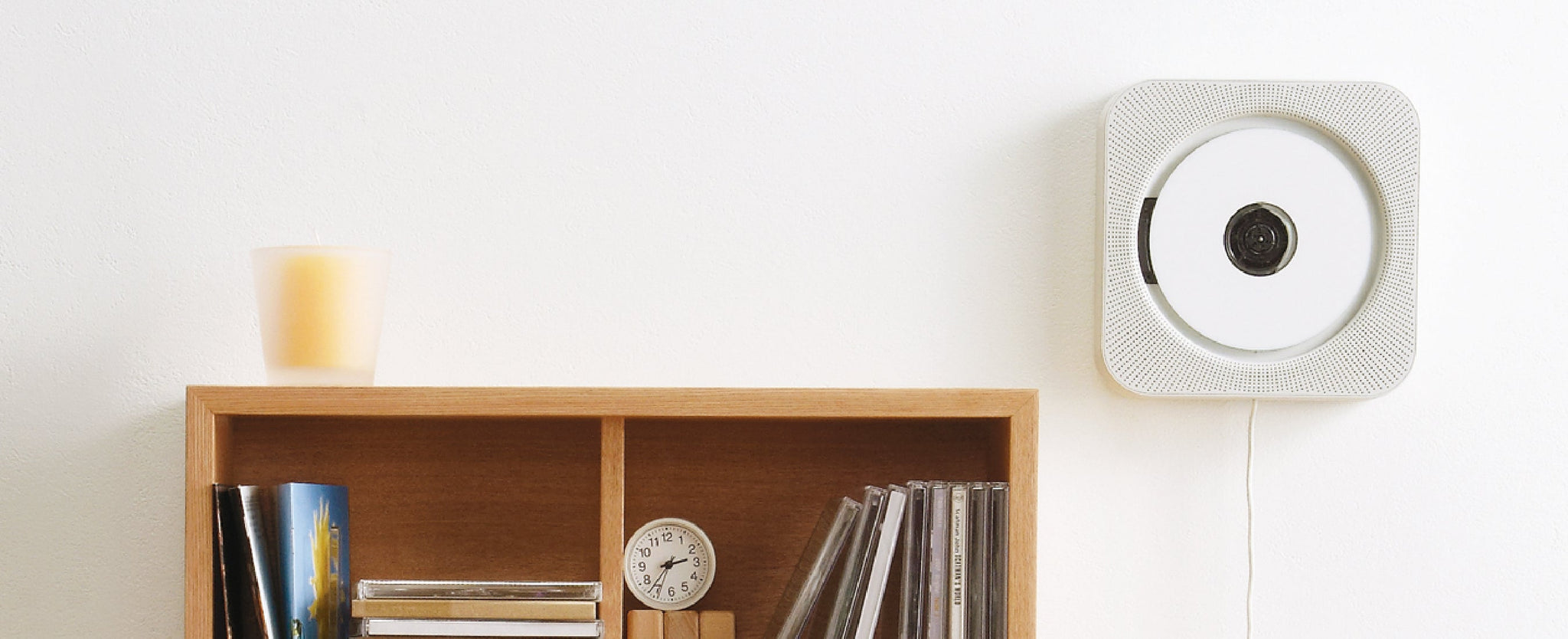 Bibliothèque en bois remplie de CD et d'une horloge, un lecteur de CD blanc est fixé au mur à droite. 