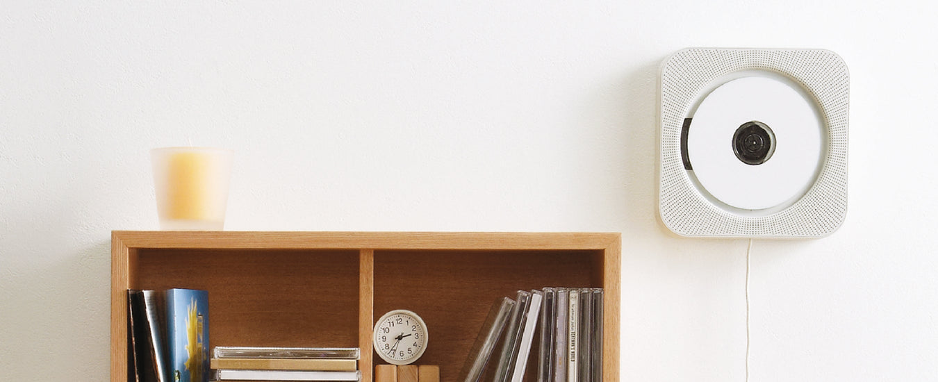 Wood Bookcase filled with CD's and a clock, a white CD player is mounted on the wall to the right 