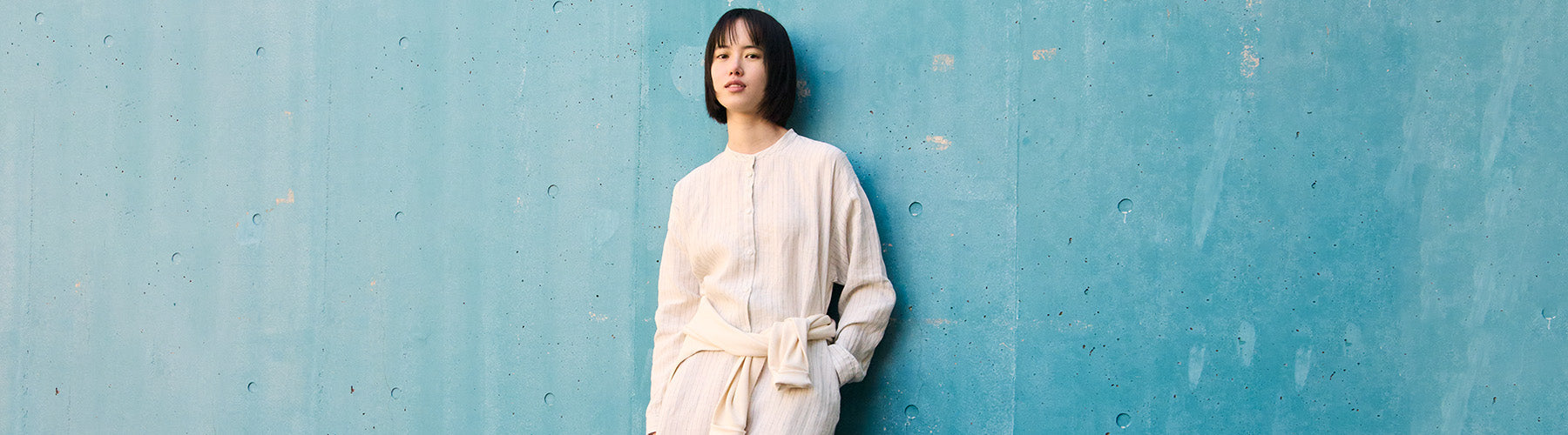 Woman wearing linen dress leaning on a blue wall. 