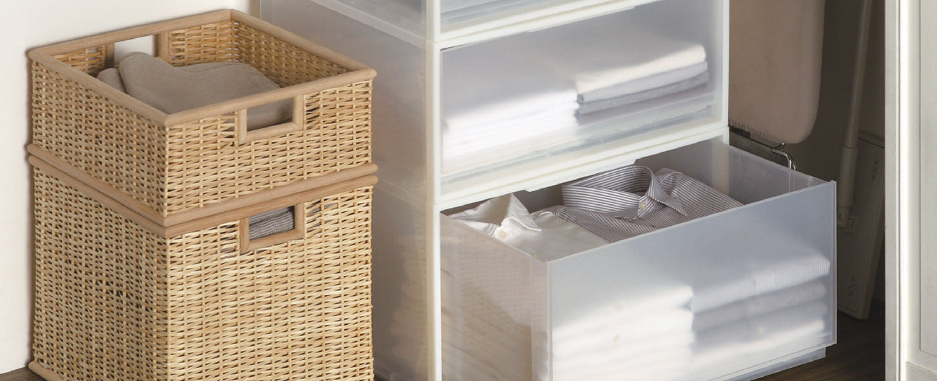 Wicker Basket next to a White Container with clear drawers.  Its bottom drawer is pulled out, in the drawer is folded button up shirts. 