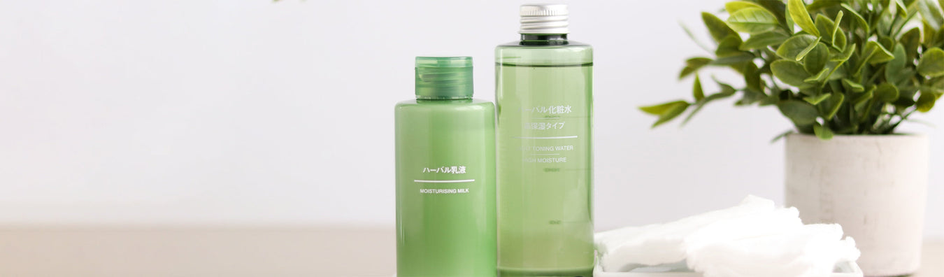 Two green bottles on a table, on the left a bottle of moisturizing milk, on the right herbal body gel. 