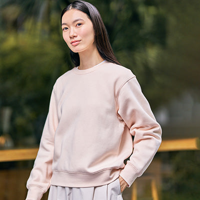 Woman wearing a light pink sweatshirt with a blurred green background