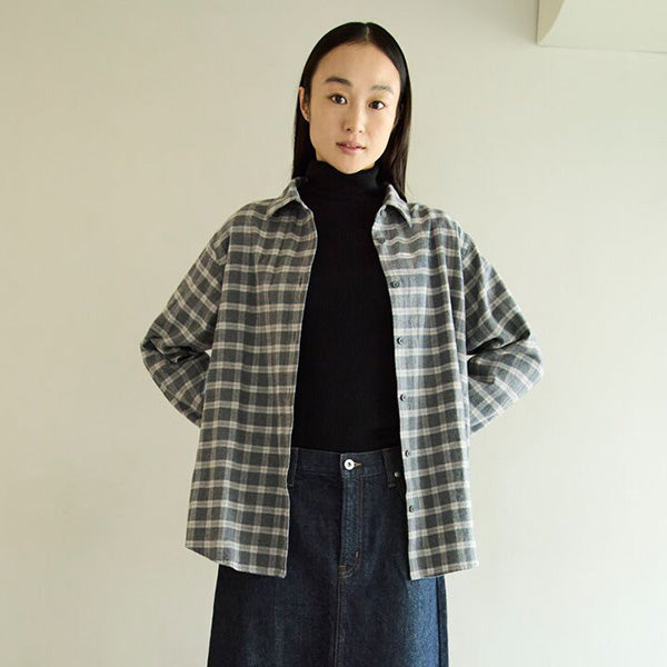 Person wearing a plaid shirt over a black turtleneck with a plain background