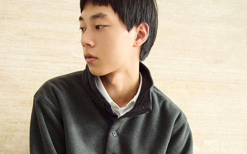 Person wearing a dark gray fleece over a white shirt against a beige background