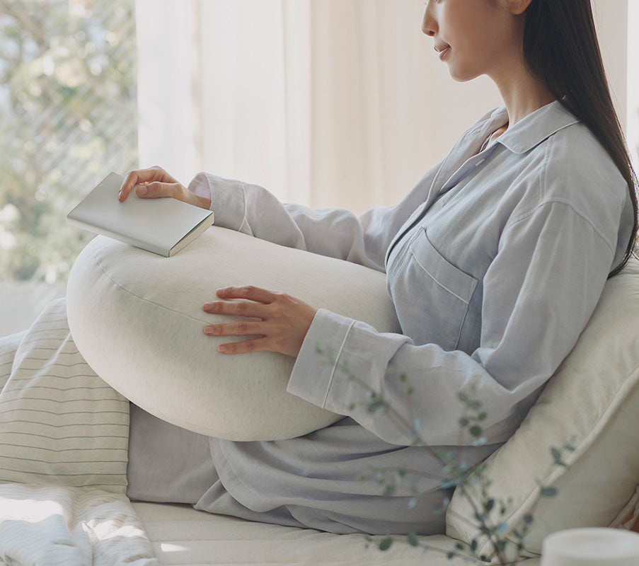 Woman Sitting in Bed with soft cushion in lap.