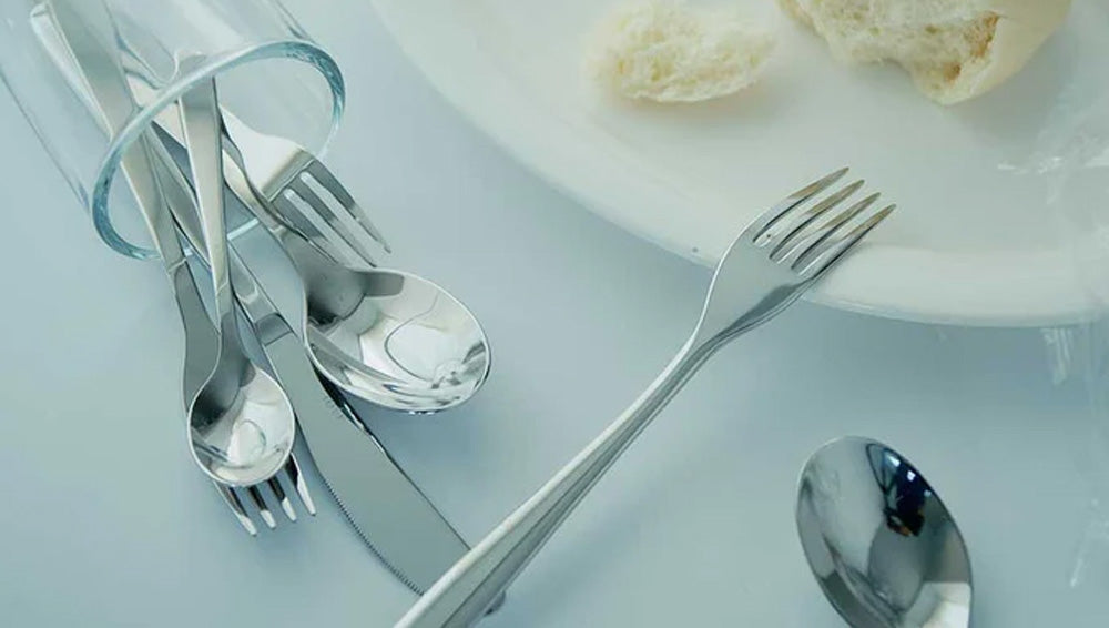 Set of IDÉE cutlery including forks and spoons on a light blue background.