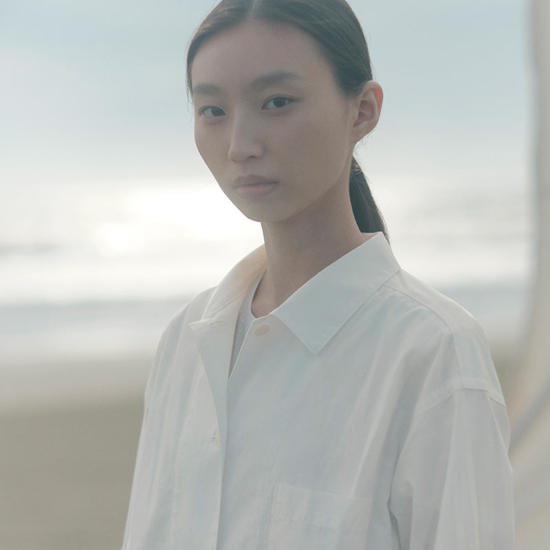 MUJI Labo - Close up of woman wearing a MUJI Labo shirt on a beach. 