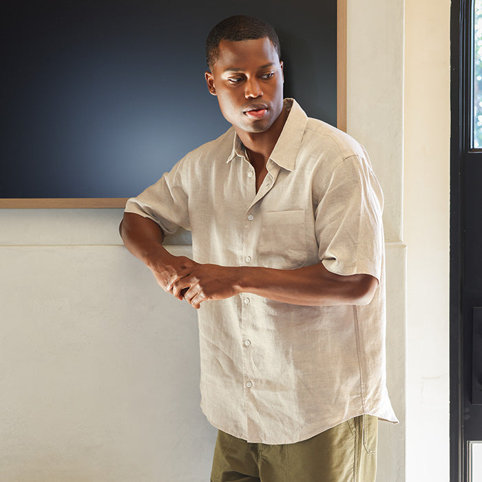 Man in a beige linen shirt standing indoors with a neutral background