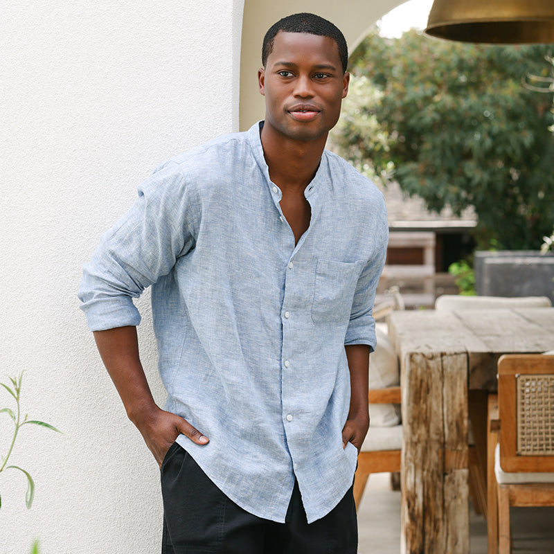 Man wearing a light blue shirt standing outdoors with greenery in the background