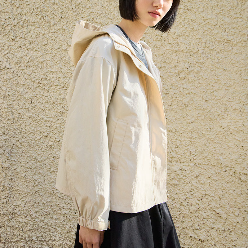 Person wearing a beige hooded jacket against a textured wall