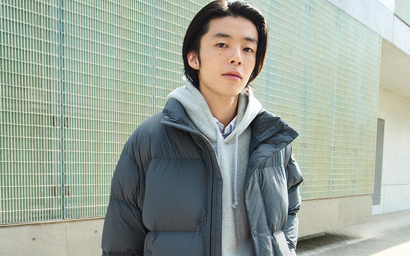 Man wearing a gray puffer jacket standing against a modern building.