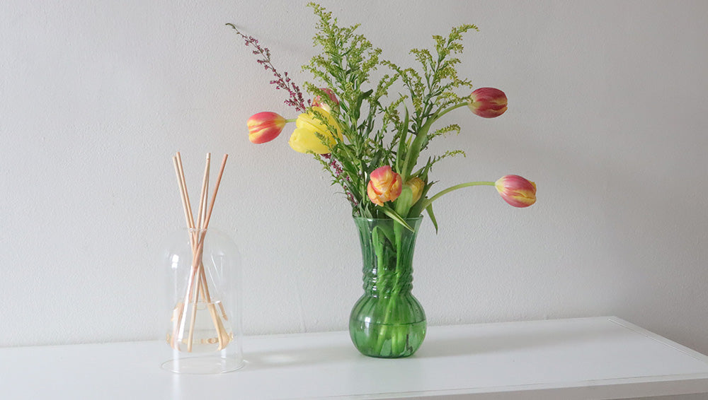 Reed Diffuser next to flowers in a vase.