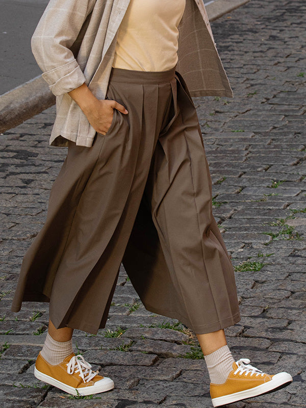 Person wearing a beige flannel, brown hakama pants, and yellow sneakers on a cobblestone street.