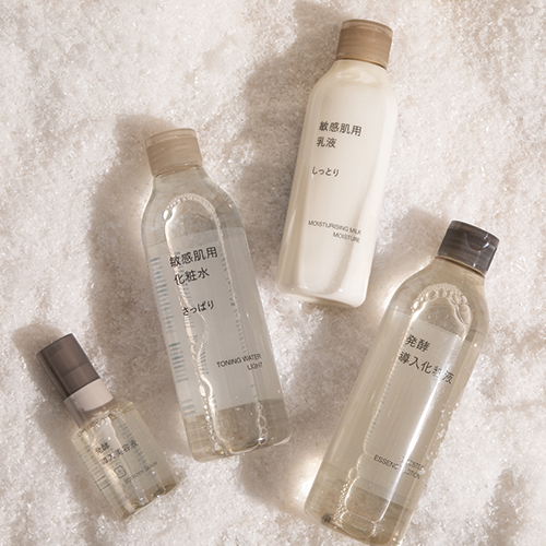 Tote bag lying flat on a white table, with two bottles of MUJI skincare products, with twinkle lights, and ribbon. 