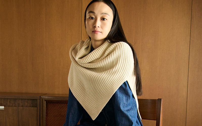 Woman wearing a beige knitted scarf against a wooden background
