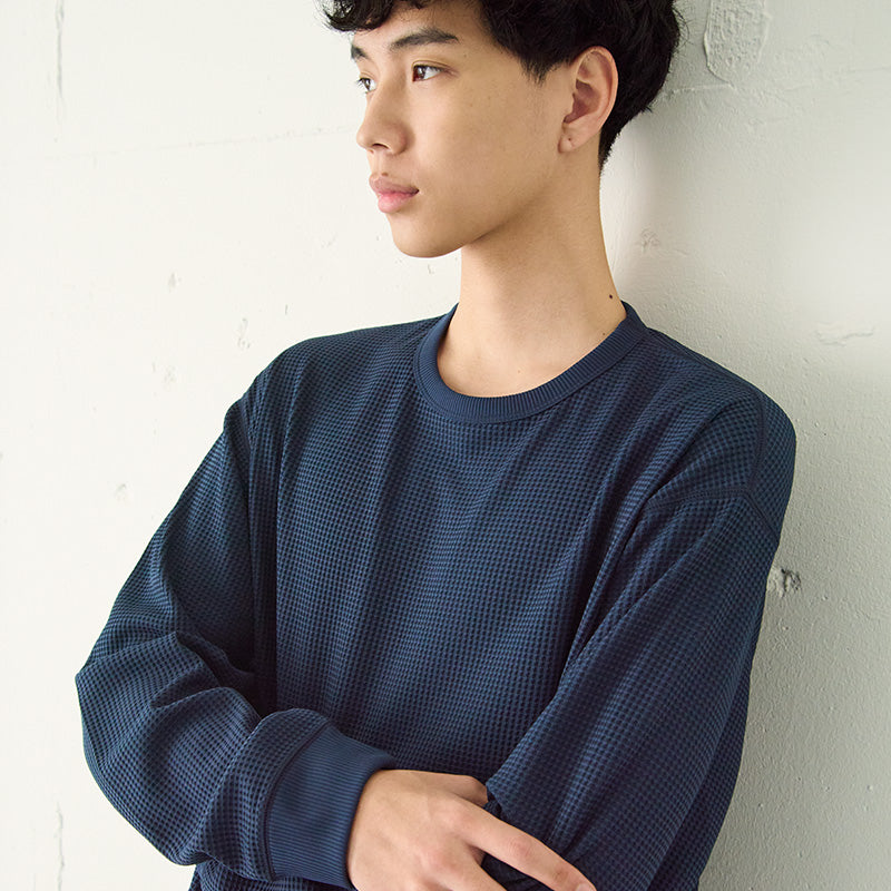 Man wearing a l/s blue waffle shirt standing with arms crossed against a white wall. 