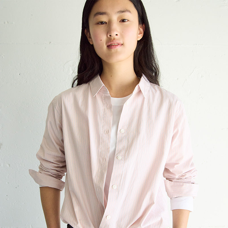 Woman wearing a pink oxford top and white undershirt. 