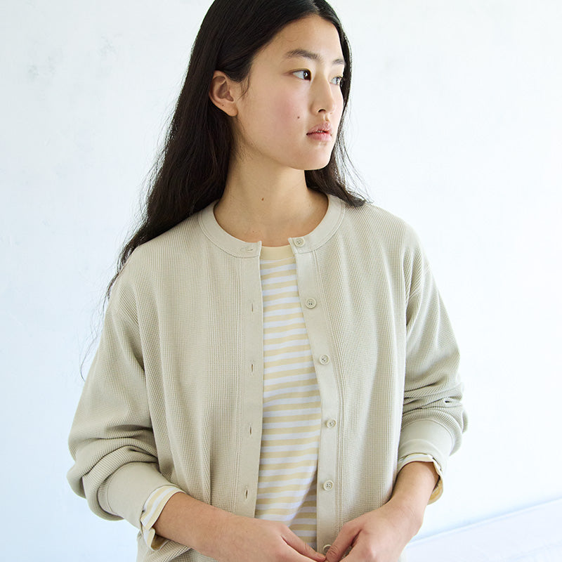 Woman wearing a light yellow cardigan and striped yellow and white t-shirt. 