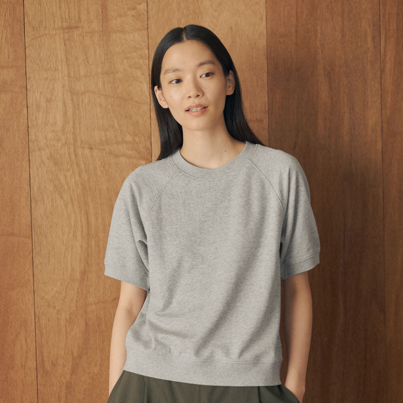 A woman with long black hair wearing a light gray heather crewneck sweatshirt